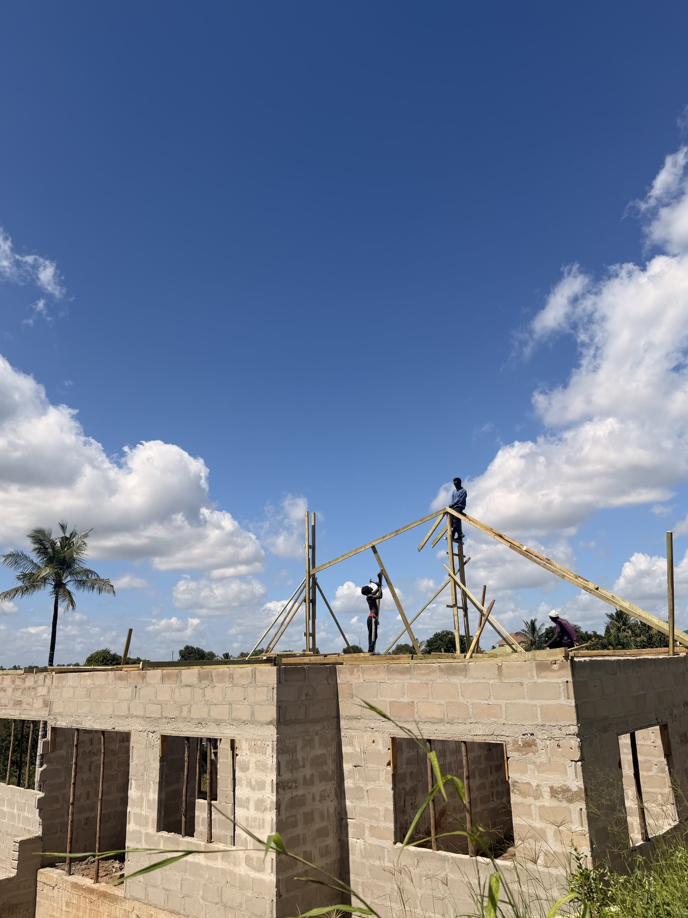 Kikwata team members erecting timber roof trusses atop a blockwork house under construction